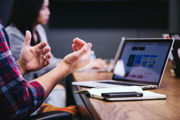 person gestures while discussing something in front of a laptop during a meeting